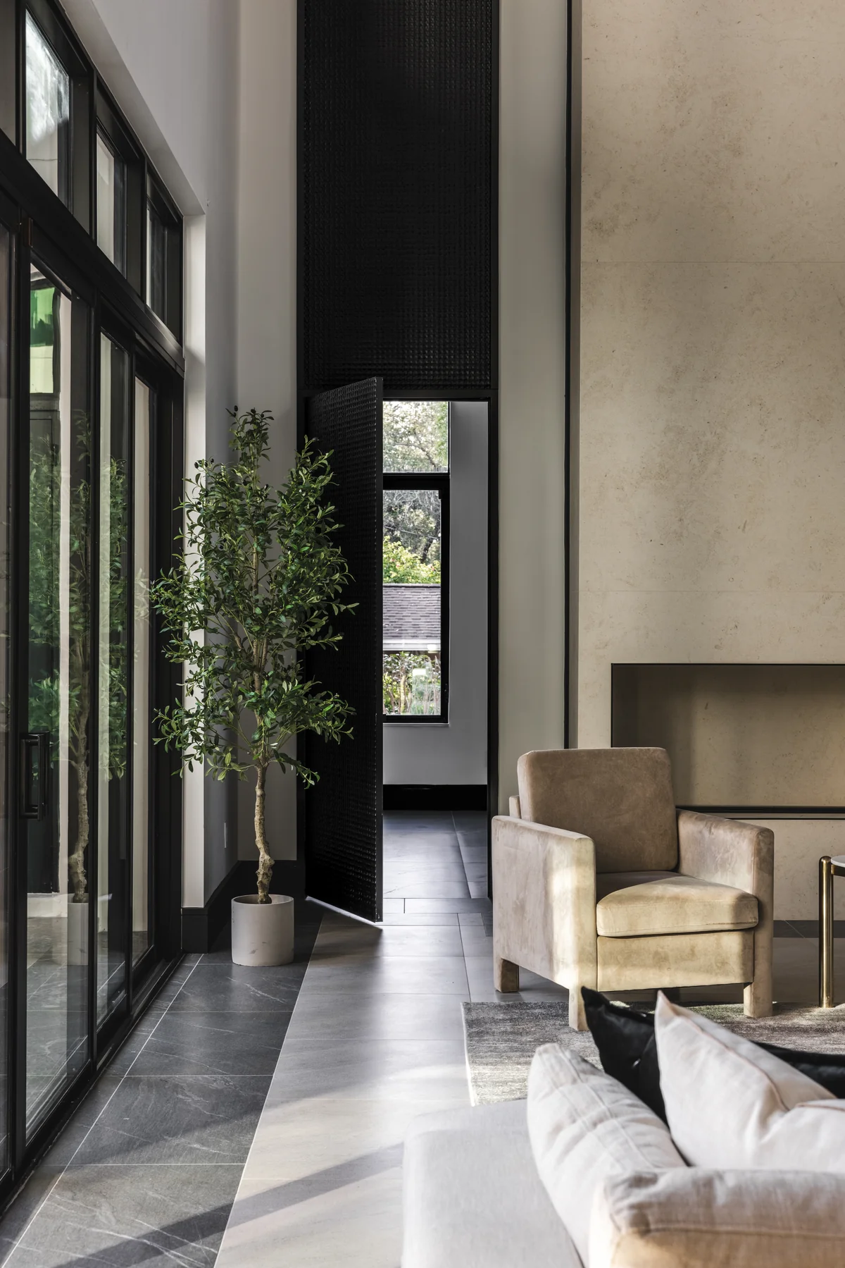 Tall living-room glazing, textured fireplace surround, and upholstered seating