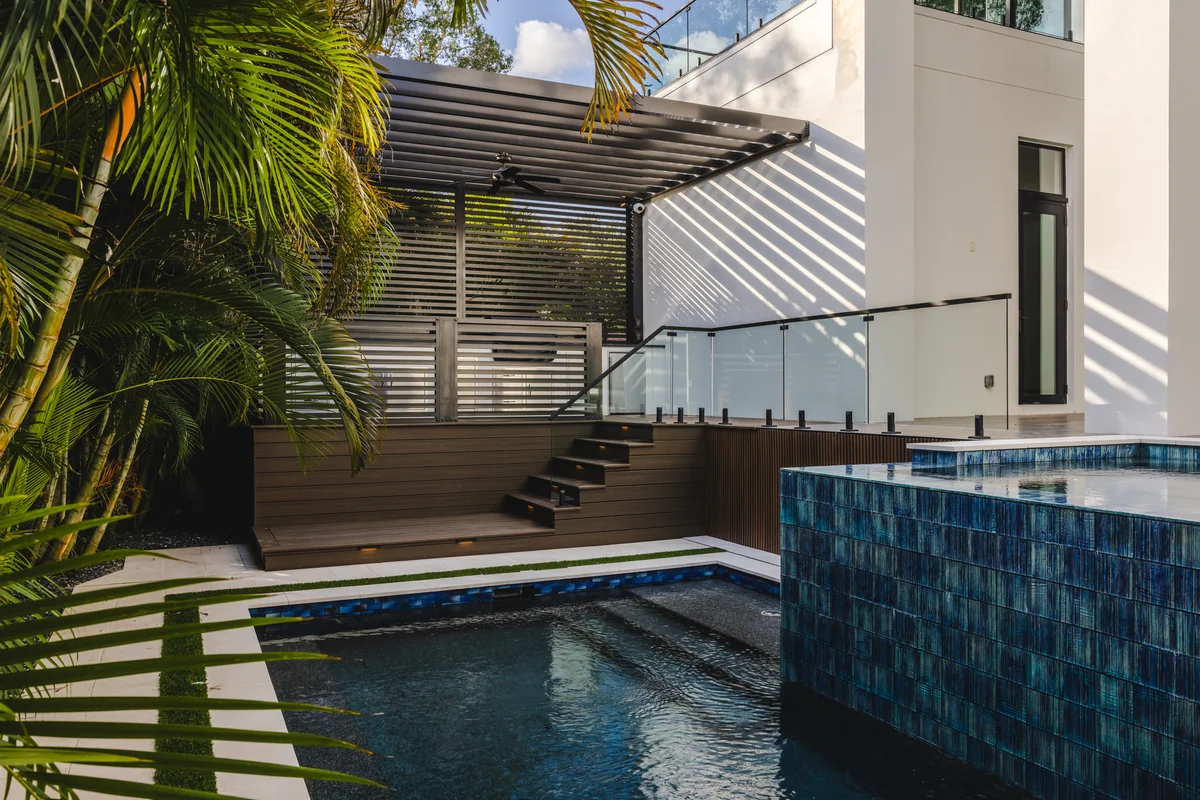 Pool and raised tiled water feature beside planted borders, paving, and a slatted shade structure
